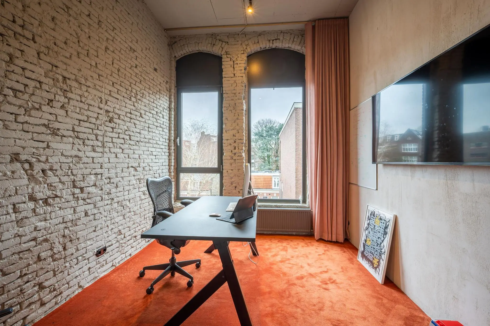 Modern kantoor met bakstenen muur, oranje vloerbedekking en uitzicht op de Admiraal de Ruijterweg.